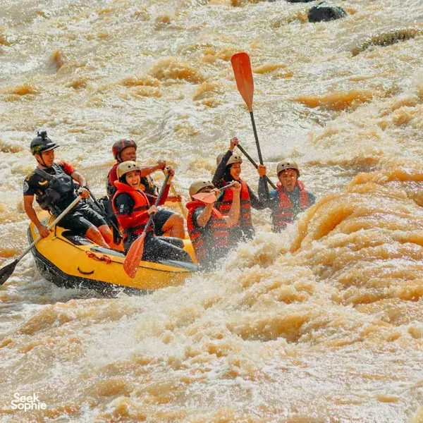 Group rafting together in an inflatable raft with paddles up, riding foamy rapids on the Padas River in Kota Kinabalu