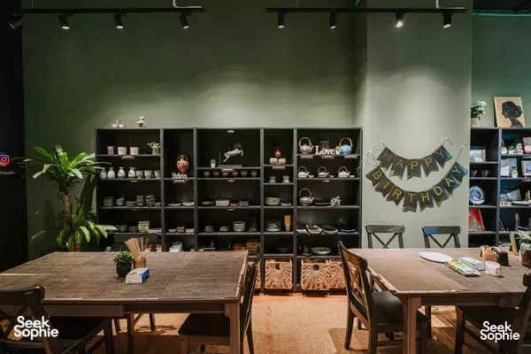 Inside Kintsugi Art Studio in Singapore, a birthday banner hangs beside dark shelving and two set tables for kintsugi classes