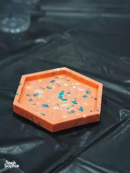 Finished orange hexagonal terrazzo coaster with colourful flecks on a table at marble & terrazzo coaster making workshops in Singapore