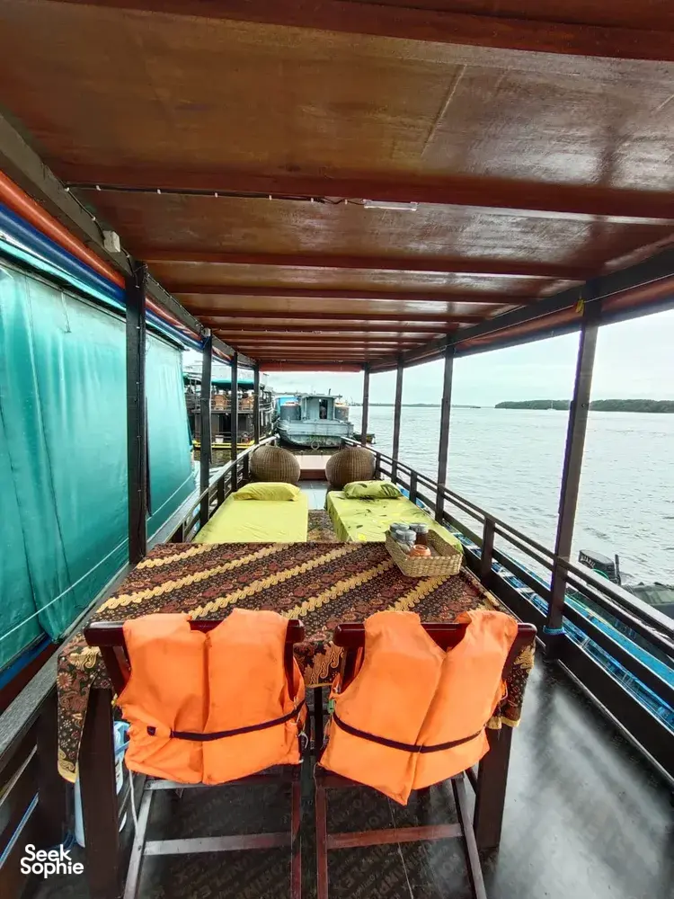 Wooden small-boat deck with bright orange life jackets and cushioned berths beside the water on a cruise in Tanjung Puting
