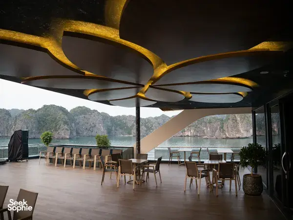 Tulip Cruise sundeck lounge with neatly set tables and chairs, framed by calm karst islets across Halong Bay