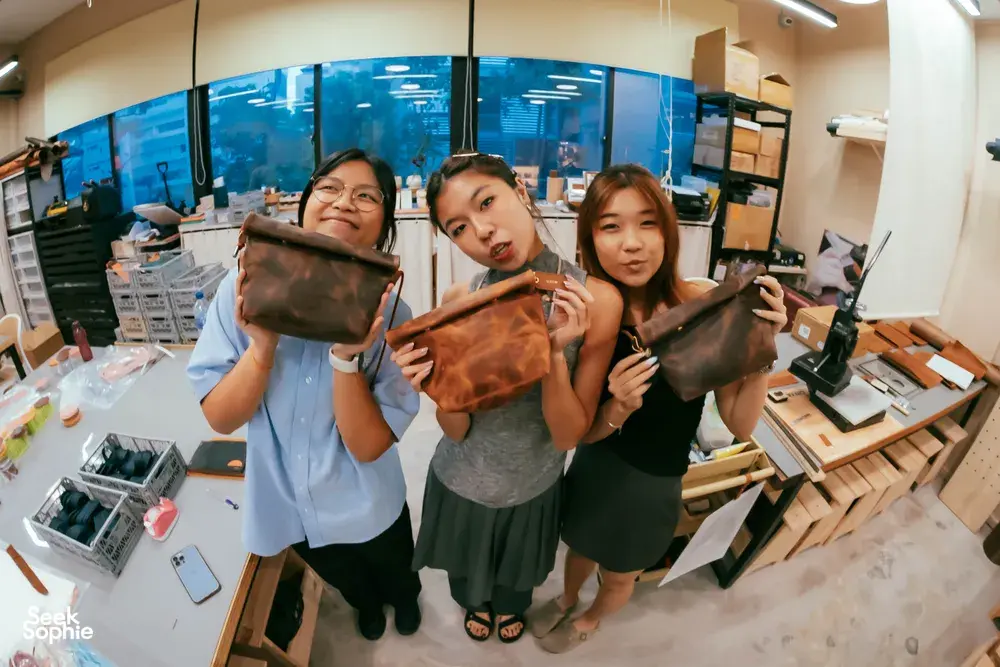 Friends holding handmade leather bags at Crafune leathercraft studio in Singapore—workshops in Singapore