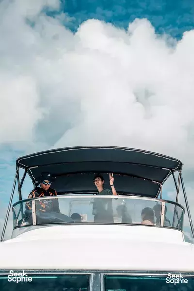 Two passengers waving from under the yacht canopy with clouds overhead, sailing the Singapore Southern Islands on a 4-hr tour