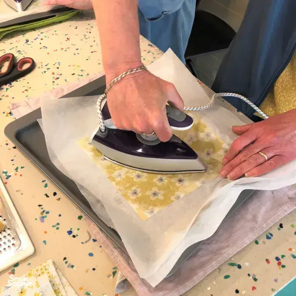 Hands ironing patterned cotton on a work mat to shape reusable food wraps for teams in Singapore during workshops in Singapore