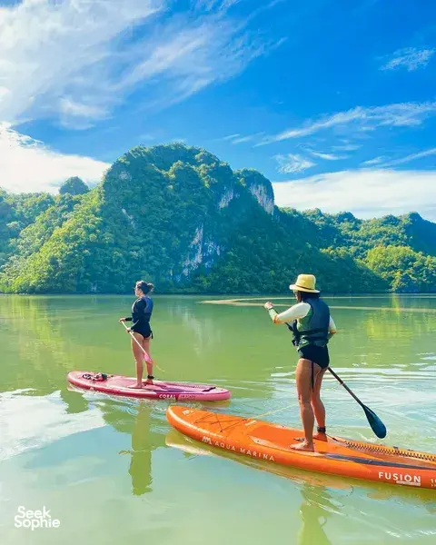 Paddleboarders cruising across glassy bay water with lush limestone hills in the distance during Tanjung Rhu SUP in Langkawi