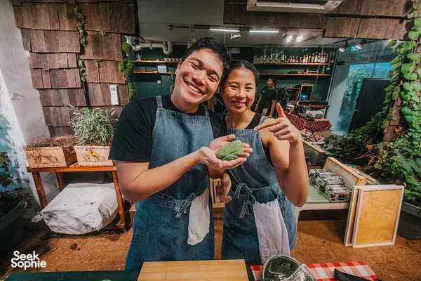 Two people in aprons smiling while holding green pasta dough at a private pasta-making & lunch in Singapore