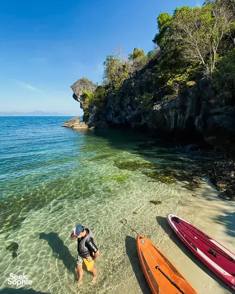 Shallow clear sea with stand-up paddleboards resting near a cliffy shoreline at Tanjung Rhu, Langkawi