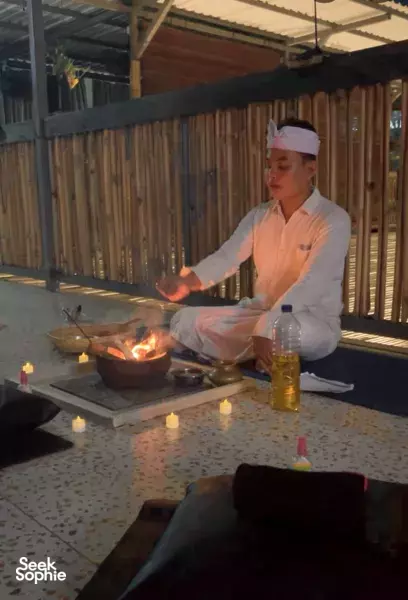 ADDA Yoga host tending an open fire and offerings on a ritual tray during a Balinese fire ritual in Canggu