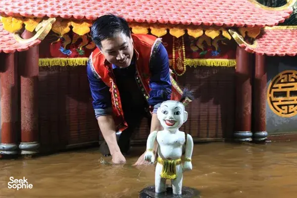 Karakter boneka air putih mini berdiri di lantai panggung sementara dalang menempatkannya di dalam teater Hanoi yang didekorasi indah