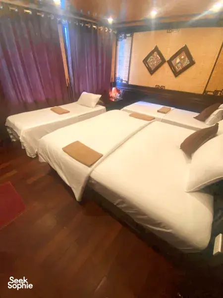 Sunlit boutique cruise cabin with two beds, soft blankets and cushions, viewed from beside the window on a Cat Ba boat, Lan Ha Bay