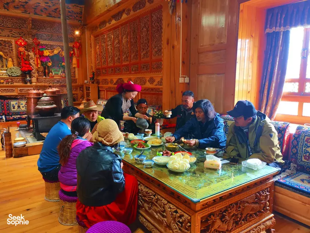 Tibetan home lunch in a warmly decorated room in Shangri-La, with travellers seated around dishes in a host-led meal