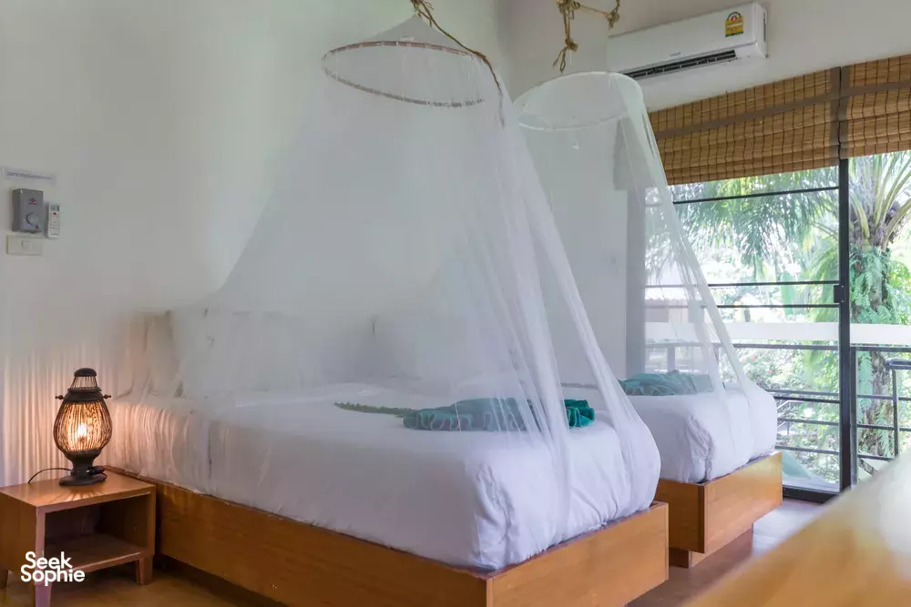 Mosquito-net canopy bed at Anurak Lodge eco-retreat in Khao Sok National Park, with balcony view through large windows