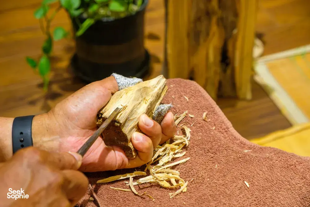 Hands hold and inspect a piece of agarwood wood on a brown cloth during a fragrance workshop in Hanoi