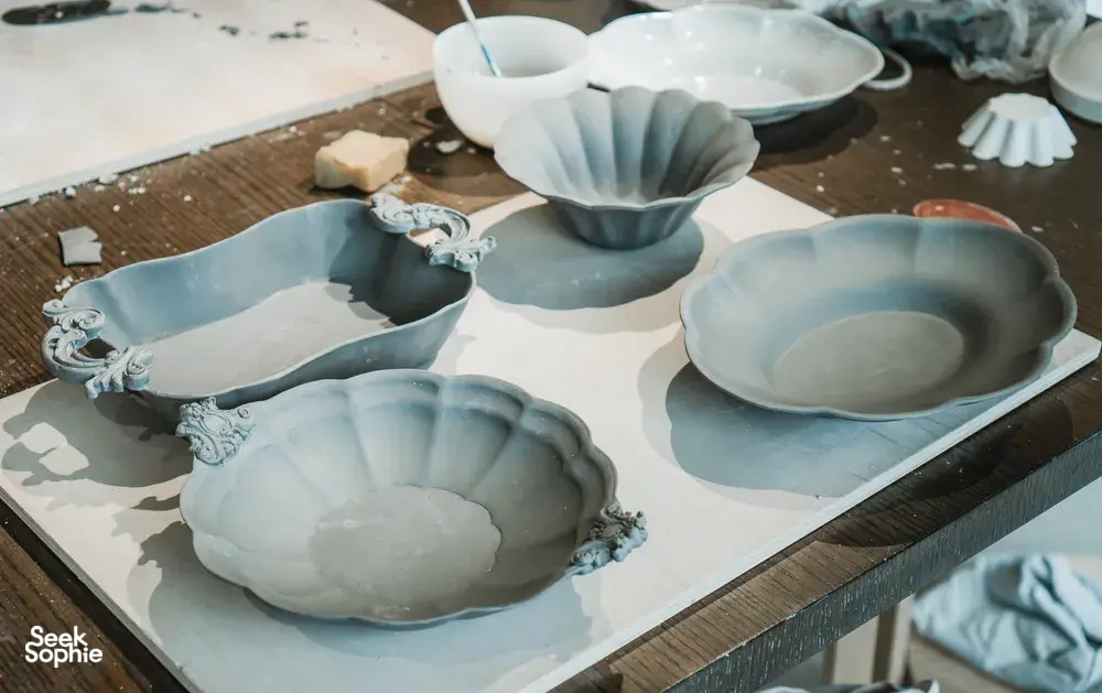 Light blue ceramic plates and shallow bowls with scalloped edges arranged on a pottery worktable at Ina Atelier workshops in Singapore