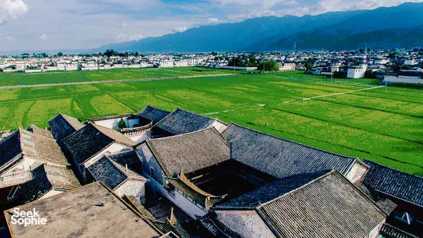 Pemandangan udara rumah-rumah beratap genting di pekan lama Xizhou, Dali, dikelilingi kehijauan sawah dan banjaran gunung di kejauhan