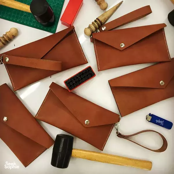 Several brown leather envelope clutches with brass snaps arranged on a crafting table with tools for workshops in Singapore
