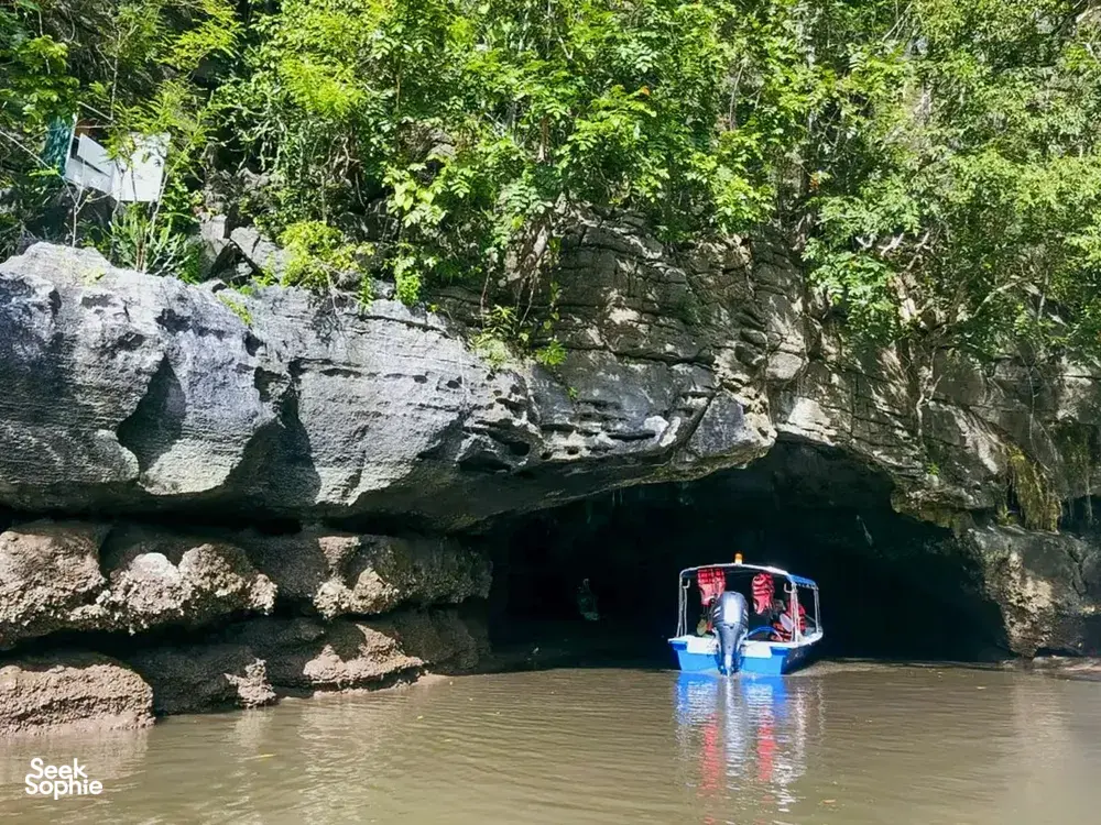 Small boat passing under limestone cliffs in Langkawi’s Tanjung Rhu UNESCO Geopark on a naturalist-guided cruise