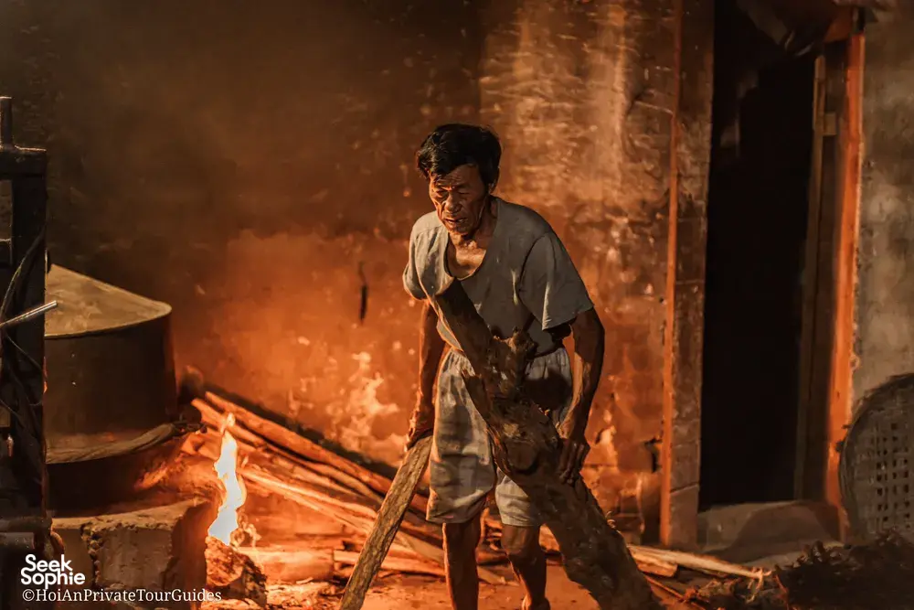Ha carrying firewood through a lantern-lit doorway in Hoi An, showing everyday trades on an early-morning tour