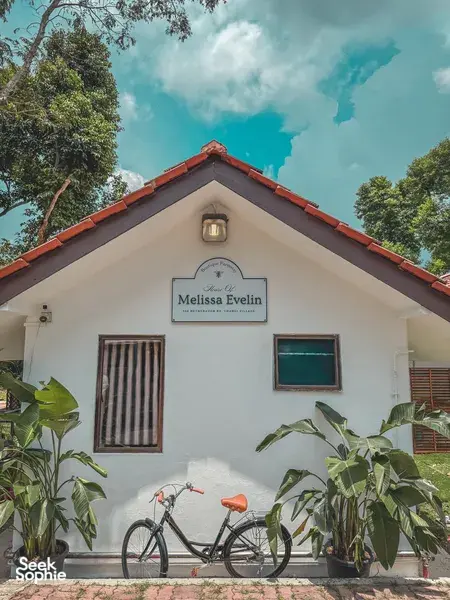 Exterior of a white bungalow with red roof tiles, a name sign and bicycle by potted plants at a Singapore farmstay by the sea