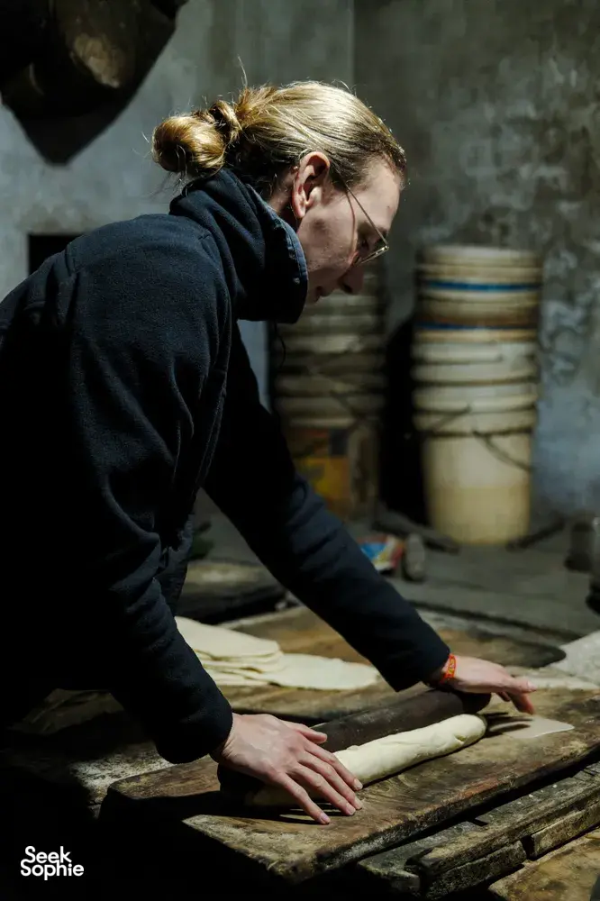 Person flattening and cutting dough on a wooden workbench inside a Hoi An workshop on an early-morning trades ride