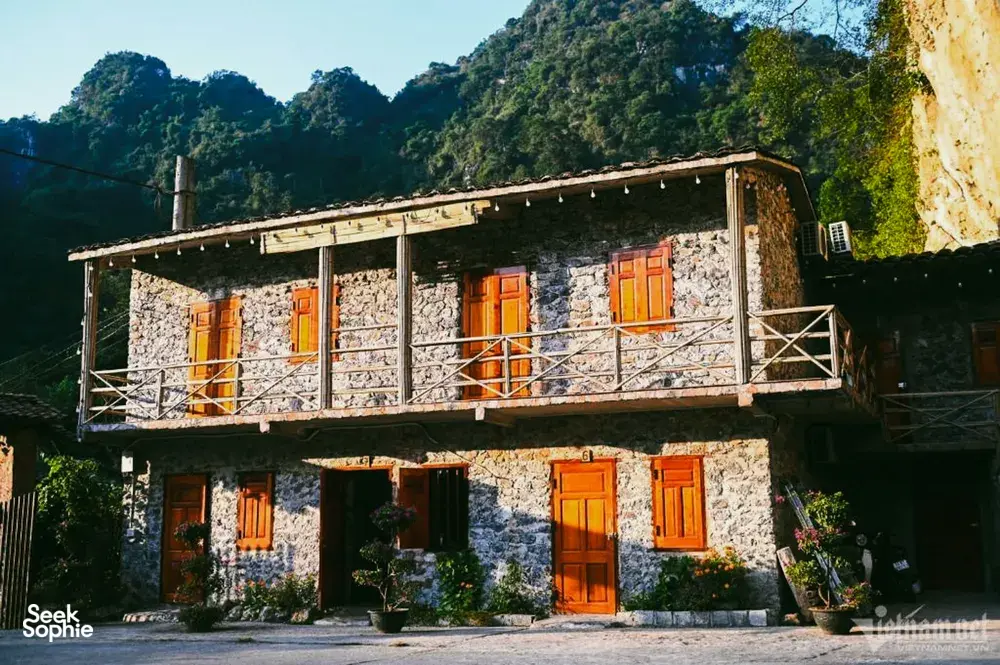 Rustic two-storey stone homestay with orange doors and a balcony in lush green hills, part of the borderland adventure