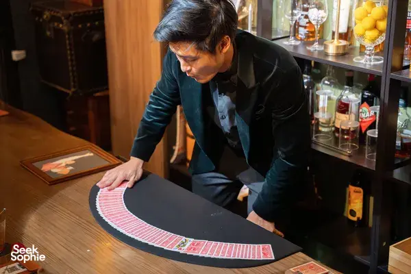 Magician leaning over a black mat with red card rows, placing cards during a Magic Workshop in Singapore at workshops in Singapore