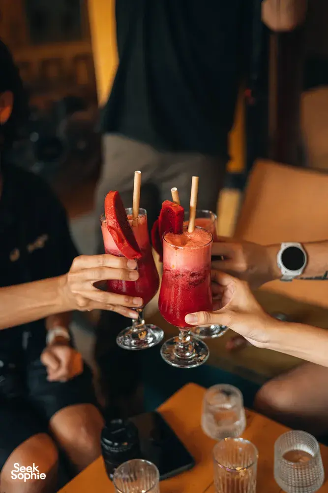 在会安的 Secret Experiences 行程中，朋友们在烛光酒吧里举起红色鸡尾酒轻碰杯，杯边点缀着西瓜角和纸吸管