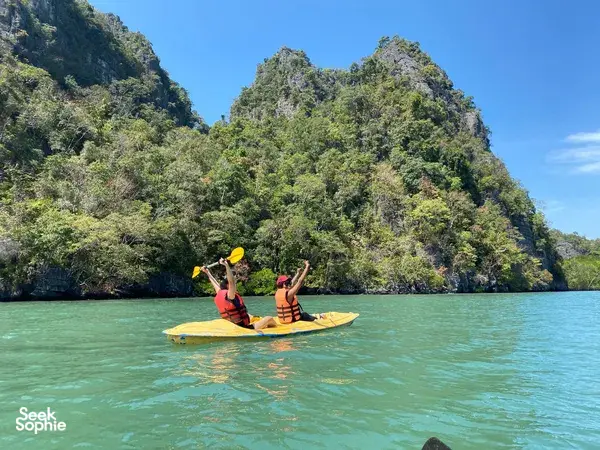 Paddlers glide across turquoise water in yellow kayaks near Langkawi’s Kilim geoforest, surrounded by steep limestone hills