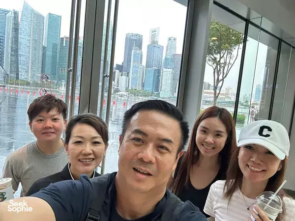 Team members taking a selfie by the window with the Singapore skyline during a Holland Village outdoor escape game — team building Singapore