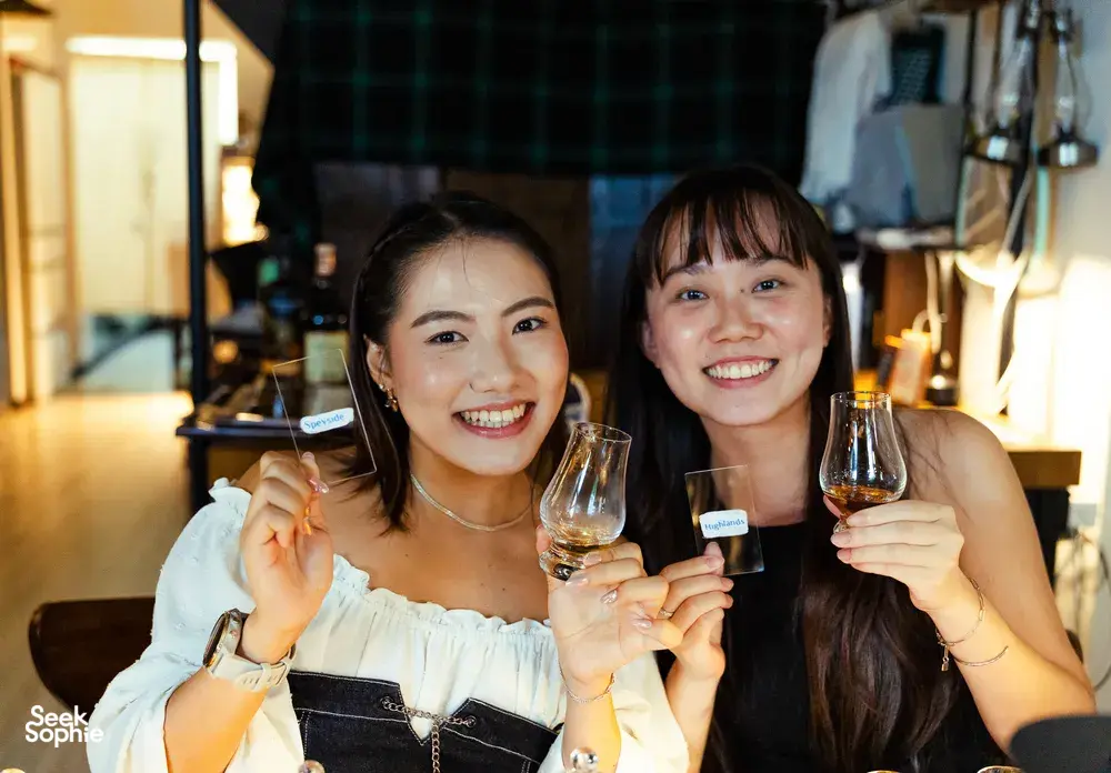 Two women smiling and toasting with small-batch whisky glasses during a host-led hidden home bar tasting in Katong, Singapore