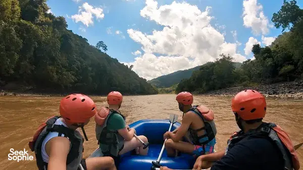Rafters in orange helmets seated on an inflatable raft on the Padas River in Sabah, looking downstream through jungle hills