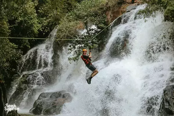 Canyoning in Da Lat: rope-assisted descent as a traveller hangs over a wide waterfall, kicking up white spray