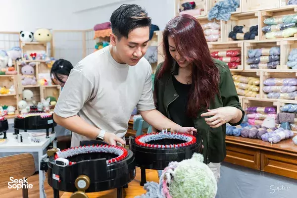 Two makers assembling plushies at sewing machines in a craft shop in Singapore with stuffed-toy shelves — workshops in Singapore