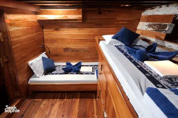 Wooden dive liveaboard cabin showing two bunks with blue towels on pillows and neatly folded blankets, in Labuan Bajo