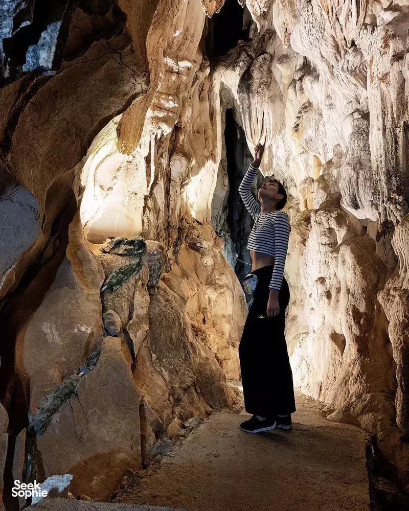 A traveller stands in a dim limestone cave during a Lyra Cruise Collection 4D3N luxury Halong Bay cruise, framed by rock arches