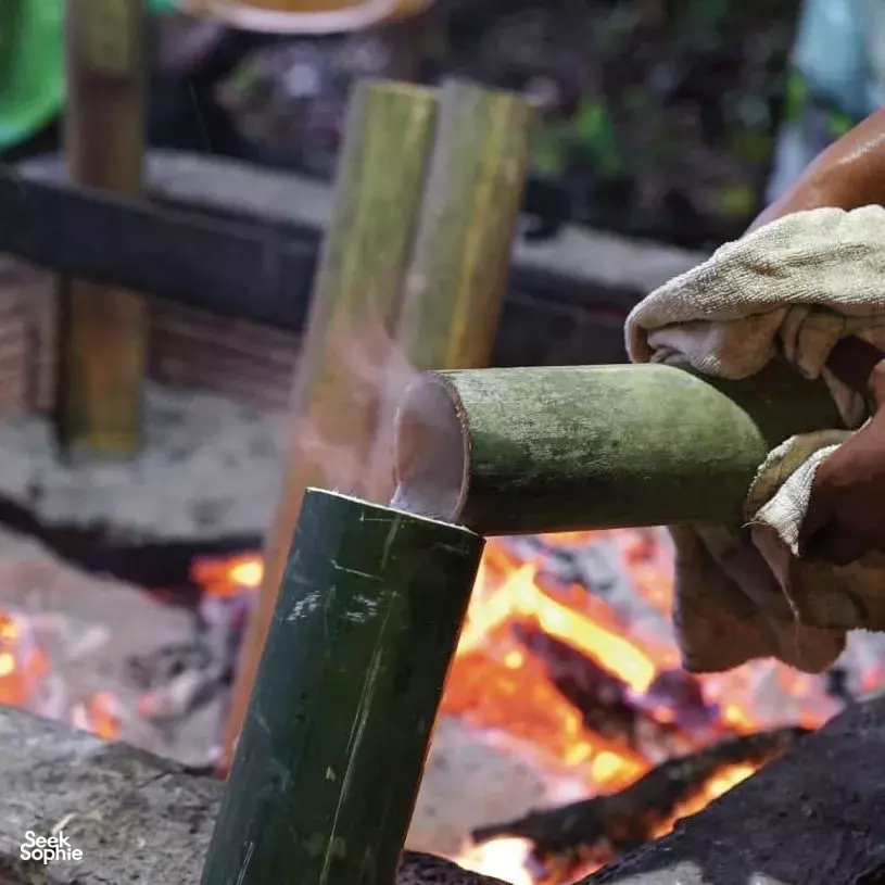 Hands chopping bamboo over a campfire during jungle dining at a rewilded rainforest stay in Khao Sok National Park