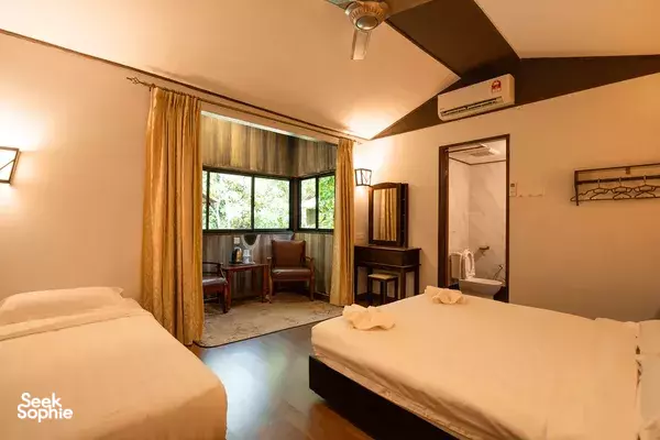 Twin beds in a simple lodge room with floor-to-ceiling curtained windows, wooden desk, wardrobe and air conditioner, Sandakan
