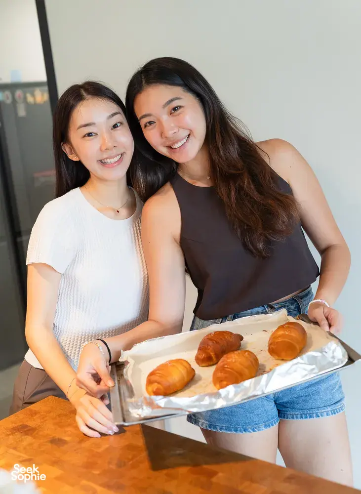 Two women smiling while sharing trays of baked shio pan buns after making flavoured butter during hands-on workshops in Singapore