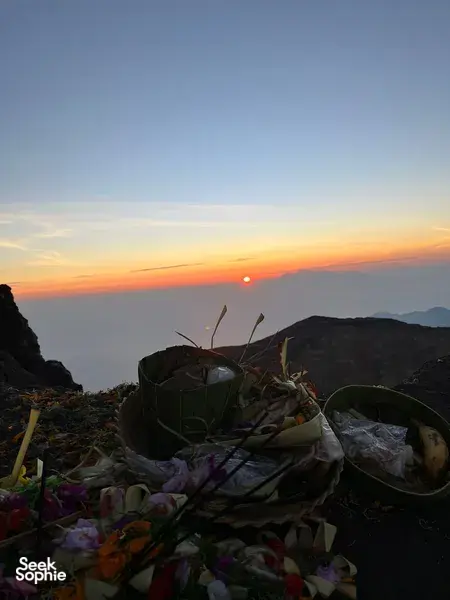 Sunrise on Mount Agung in Bali with flower offering baskets arranged on summit rocks in the foreground during a private trek