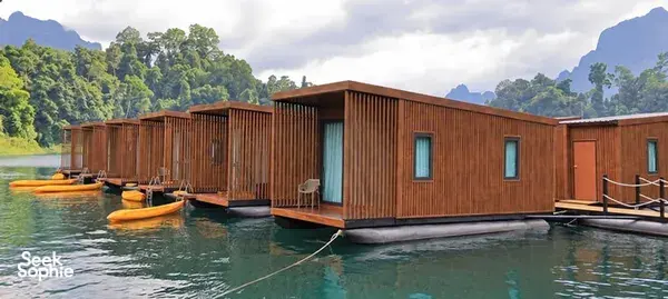 考索国家公园湖面上的棕色木质漂浮露营小屋,配有蓝绿色窗帘和一条小栈道