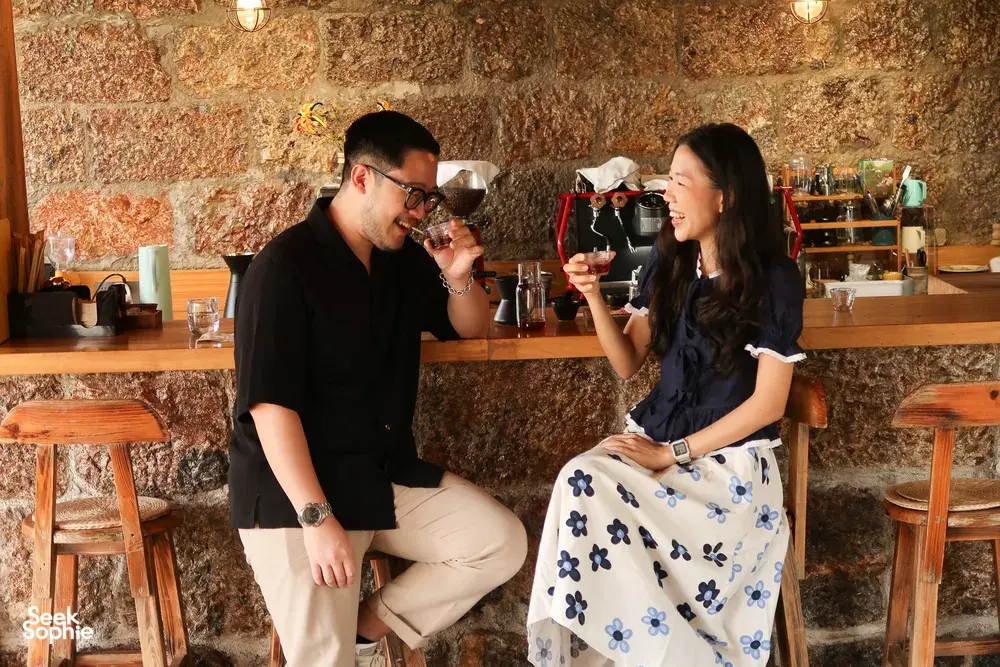Yunnan coffee tasting in Lijiang at a stone-walled bar, two people drink from glasses surrounded by brewing tools