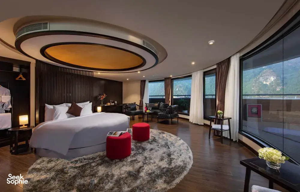Luxury bedroom on the Oasis Bay Party Cruise with a round ceiling light, bedding and large windows over Halong Bay