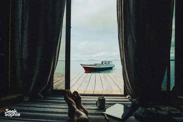 Curtains open inside a sea-lodge cabin at Semporna, looking out at a boat moored beside the wooden pier