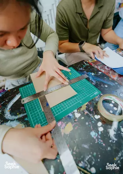 Hands using a ruler and craft knife to cut patterned leather on green cutting mats during workshops in Singapore