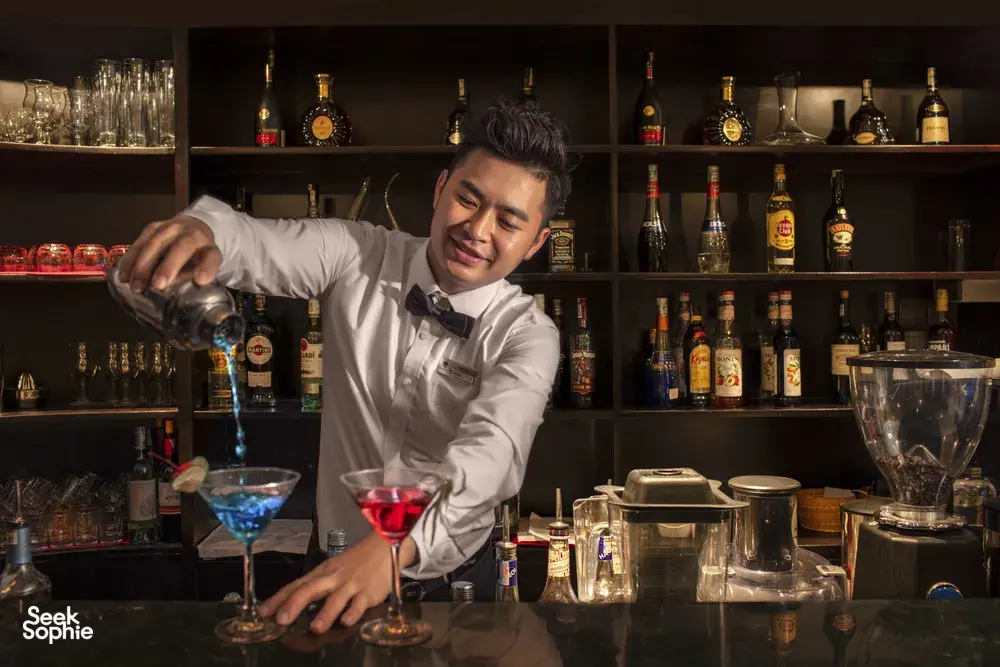 Oasis Bay Party Cruiser bartender shaking and pouring cocktails behind a bar of bottles on a Halong Bay cruise