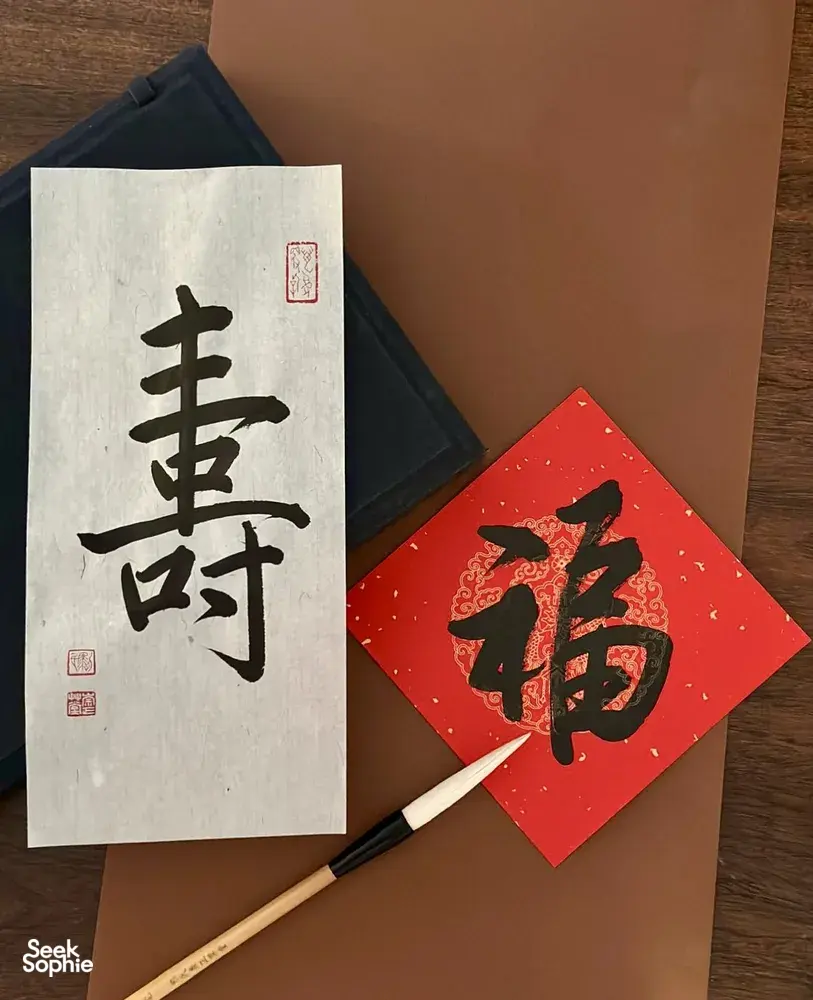 Chinese calligraphy sheet with bold black characters, a brush and red envelope on a wooden table for calligraphy workshops in Singapore