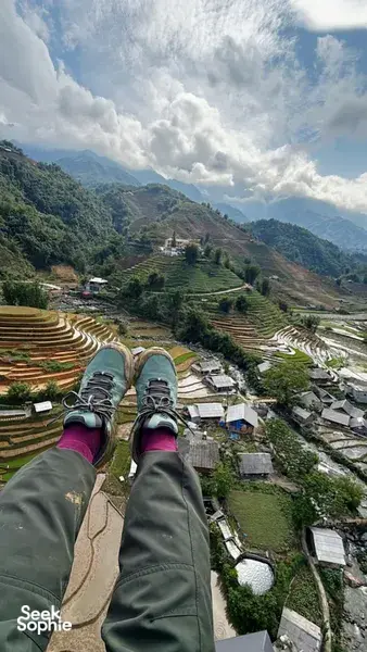 Paragliding passenger view over terraced rice valleys and mountain village paths far below, with clouds overhead, above Vietnam's Sapa