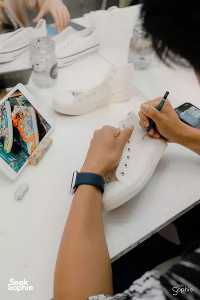Hands decorating white canvas sneakers with paint pens on a craft table during a sneaker art session for workshops in Singapore
