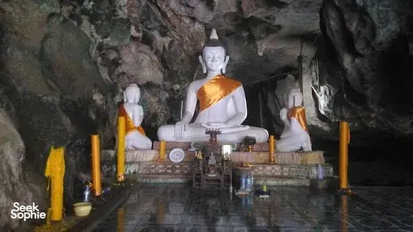 Buddha shrine altar with three seated statues and candles in a rocky cave on a Khao Sok ex-poacher trek in Khao Sok National Park