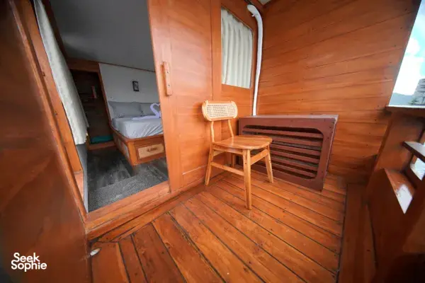 Travass Life 3D2N join-in Komodo trip wooden cabin lounge with a chair, mirror and tucked-away bed, Labuan Bajo